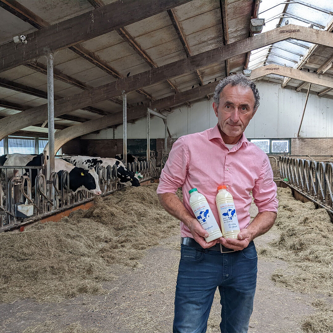 boer Arnold van Adrichem met 2 flessen zuivel van Delflandshof in een stal met koeien in Midden-Delfland maker streekproduct zuivel melk yoghurt