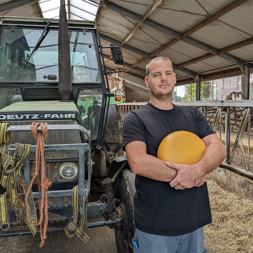 Boer Bas van den Berg van Hoeve Ackerdijk staat voor een traktor in de schuur op zijn boerderij Hoeve Ackerdijck in Midden-Delfland met in zijn handen een grote ronde gele kaas streekproduct van de melk van zijn eigen koeien maker