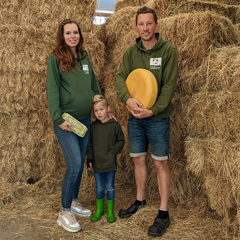 Roel van Buuren met zijn vrouw Femke en zoontje Levi in een schuur met hooi en een grote ronde gele kaas en een doosje eieren van hun Boerderij Landlust in Midden-Delfland boer maker streekproducten