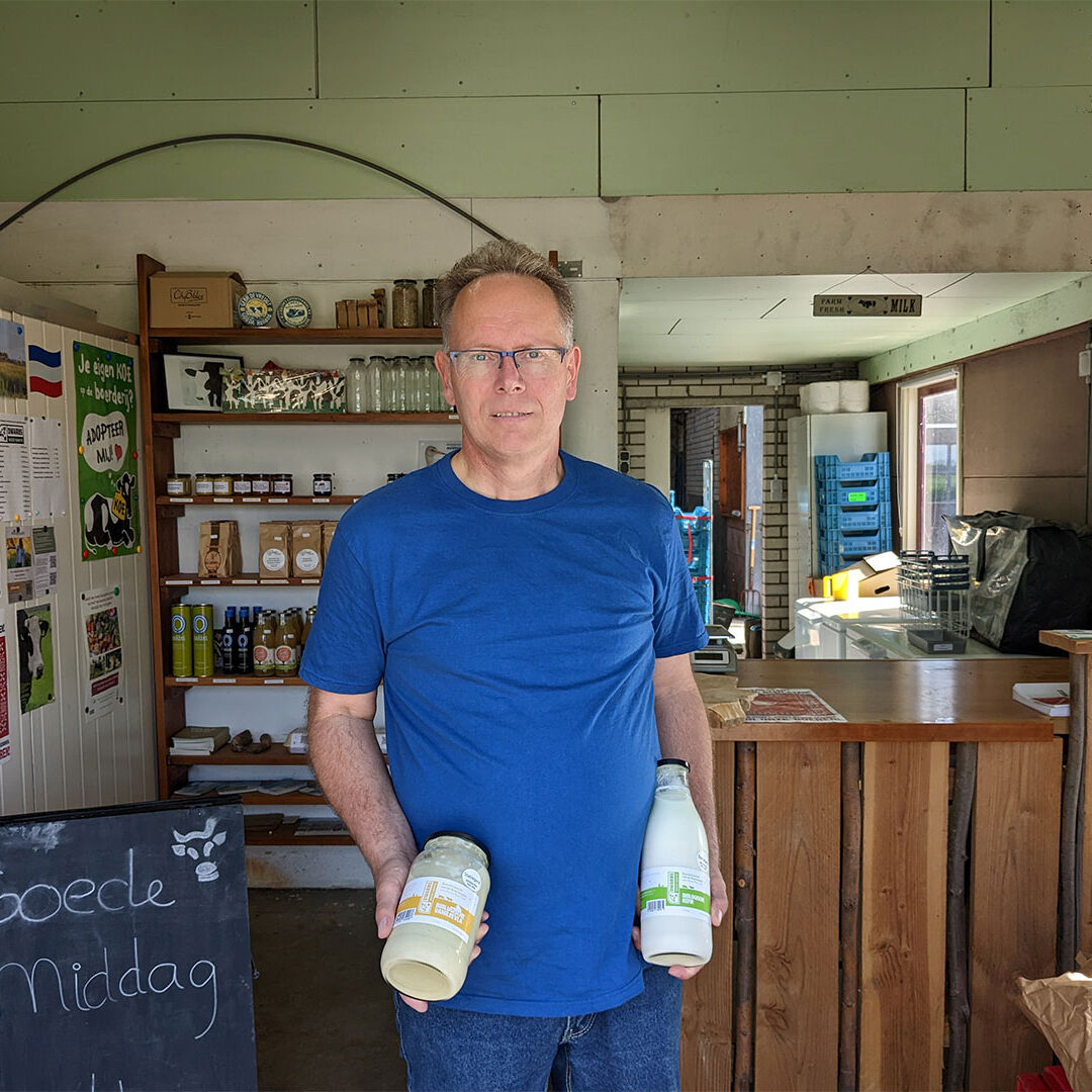 portret van boer en maker Jeroen van der Kooij van Hoeve Rust-hoff in de boerderijwinkel op zijn boerderij in Midden-Delfland met in zijn handen een fles boeren vanillevla en een fles kefir gemaakt van zijn eigen biologische melk
