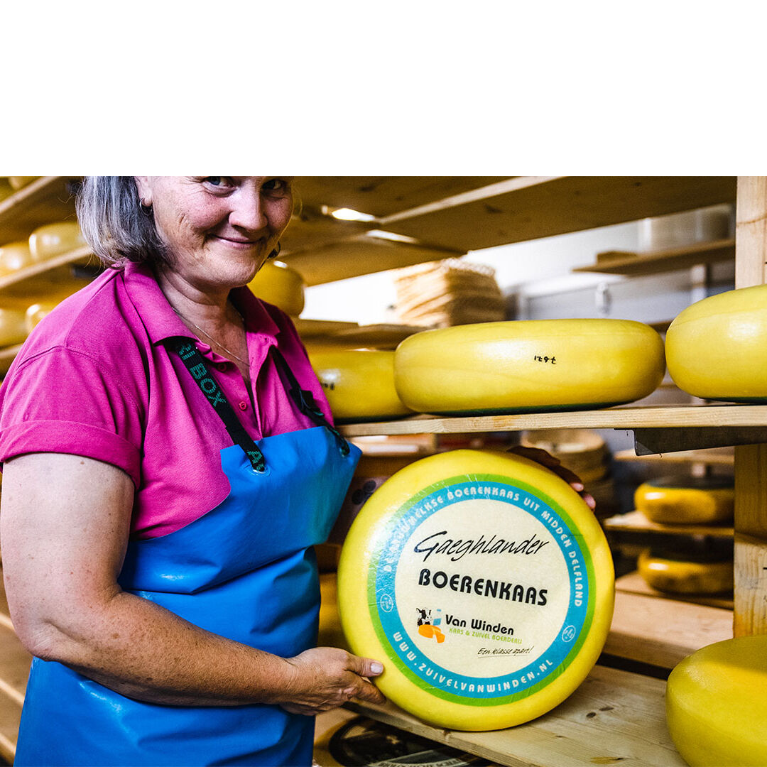 Boerin Nelly van Winden van Kaas- en zuivelboerderij van Winden uit Midden-Delfland met een grote gele kaas van haar eigen boerderij streekproduct boerenlandwinkel maker