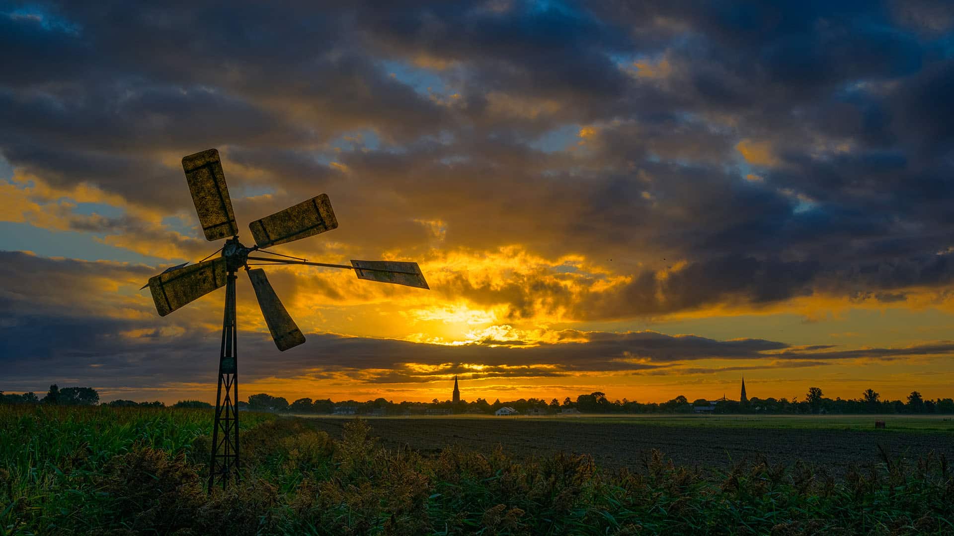 weide met opkomende zon en wolken met een windmolen in Midden-Delfland