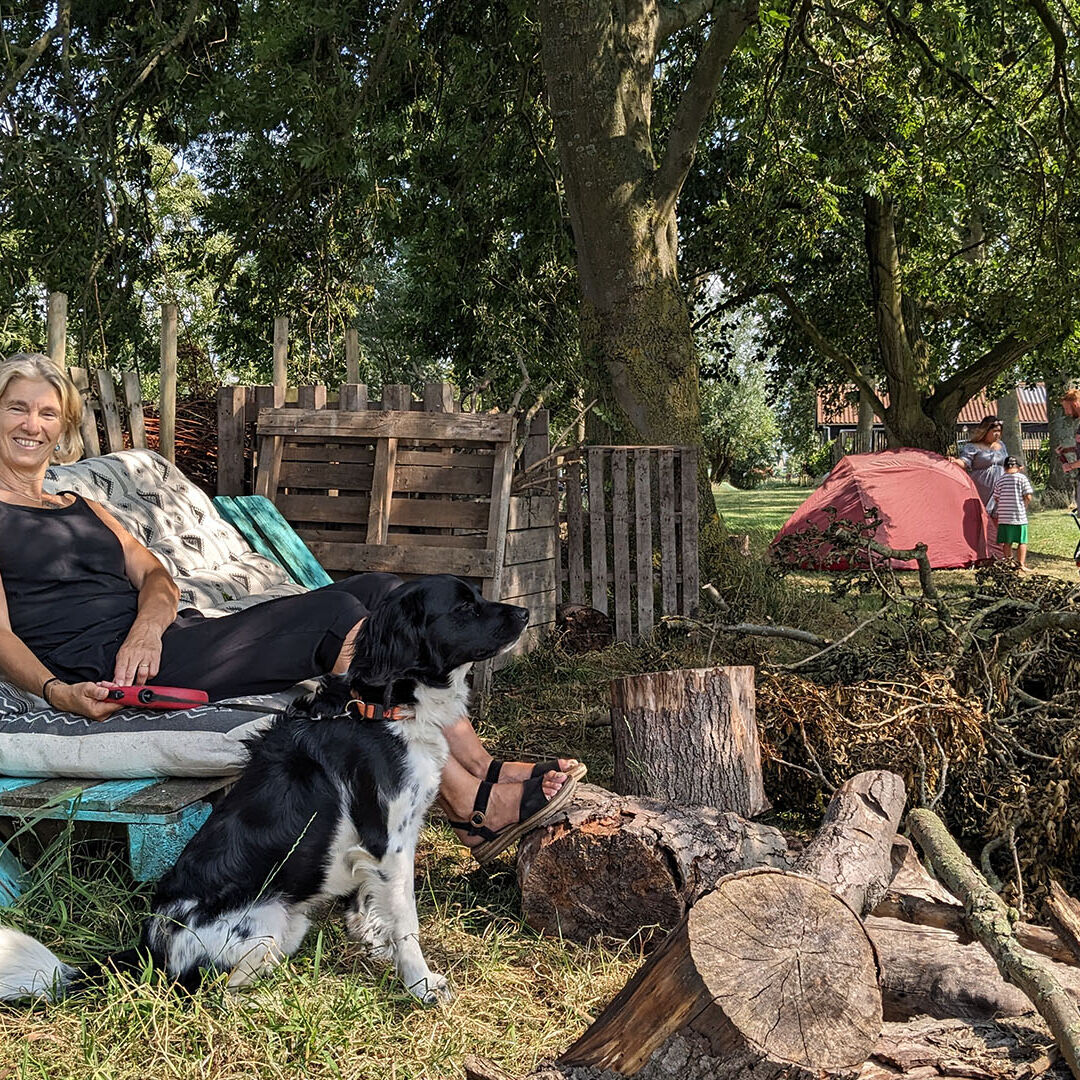 Angela met hond Guus bij de vuurplaats van camping Buitenplaats Ta Fête met een stapel hout voor op het vuur in Midden-Delfland