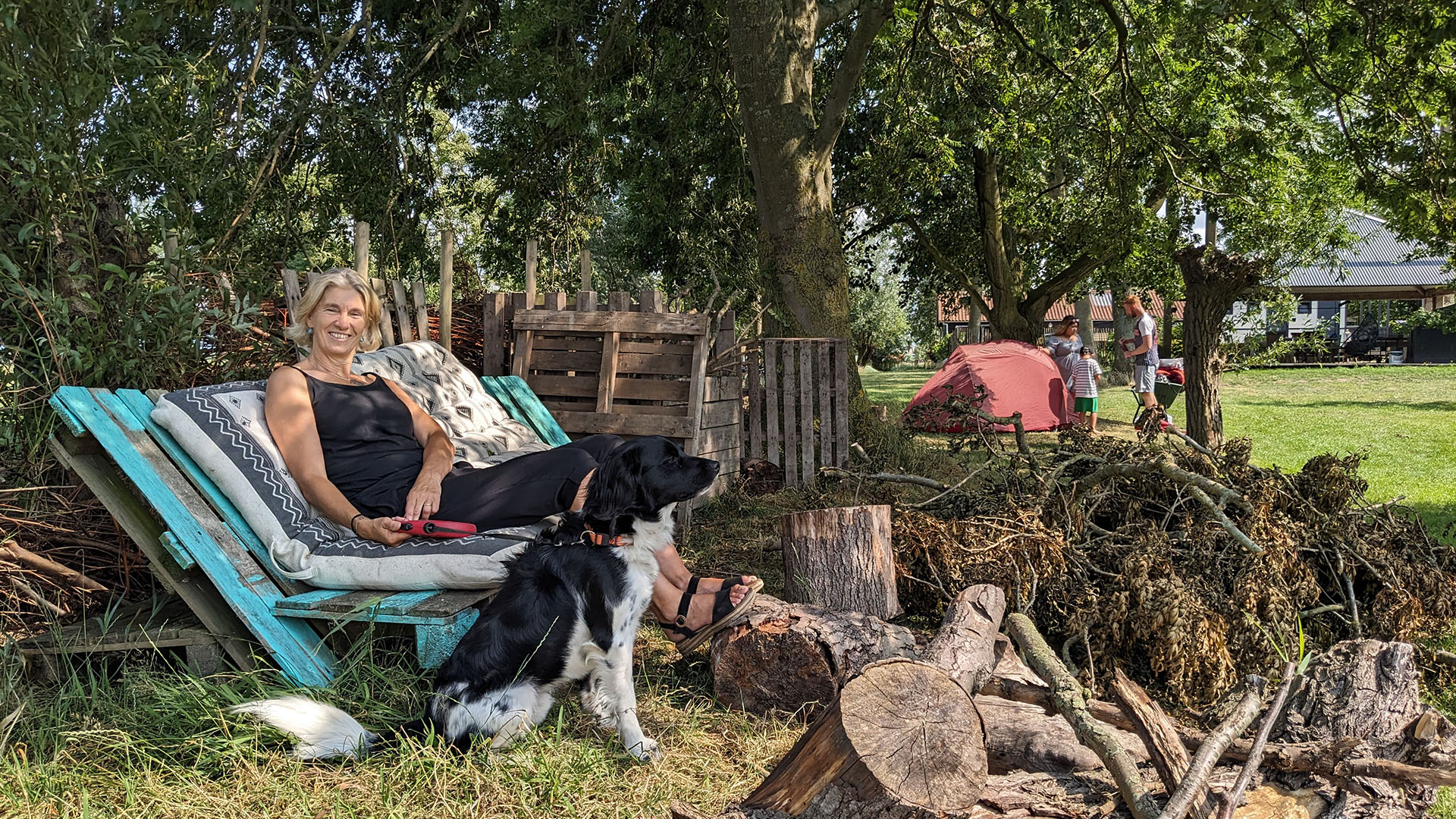 Angela met hond Guus bij de vuurplaats van camping Buitenplaats Ta Fête met een stapel hout voor op het vuur in Midden-Delfland