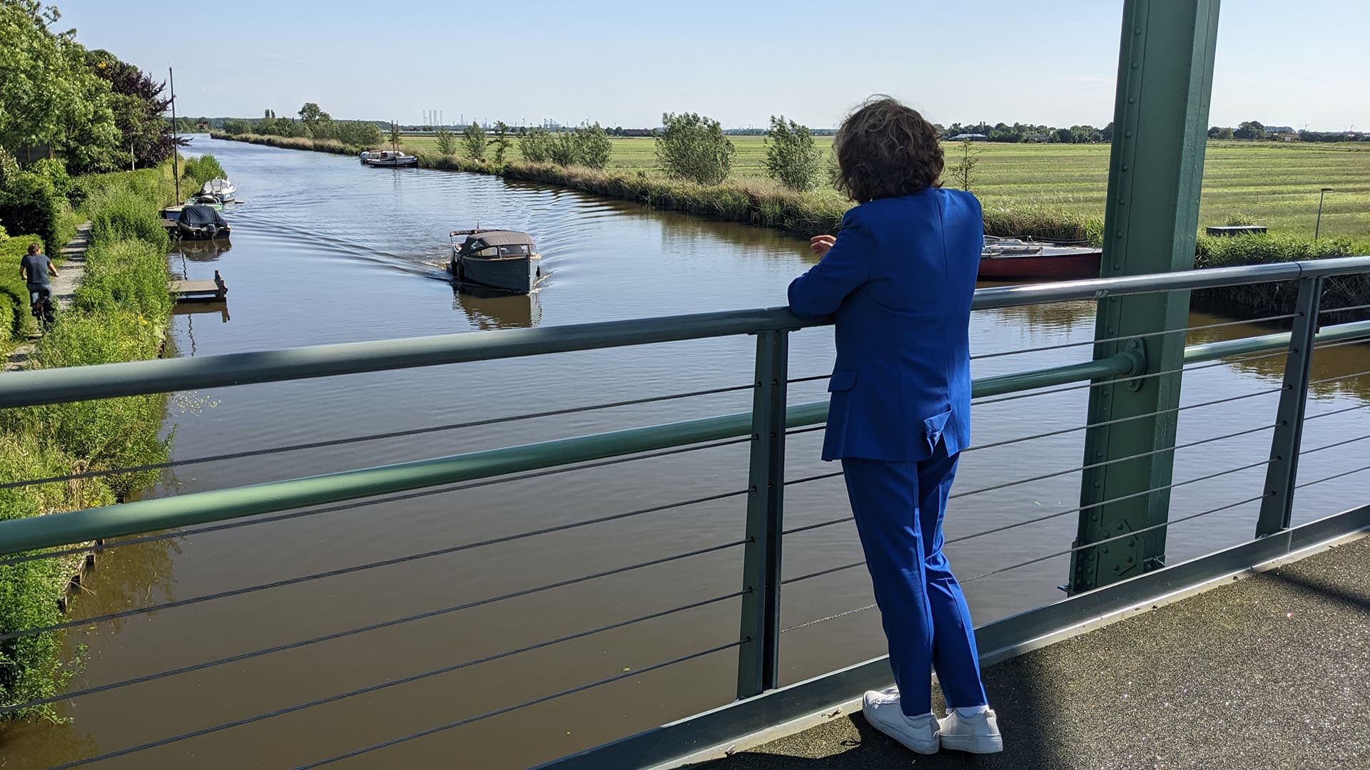 Marja van Bijsterveld op de trambrug in Schipluiden uitkijkend over de Vlaardingsevaart en een aankomend bootje op een zonnige dag voor de column MD door de ogen van